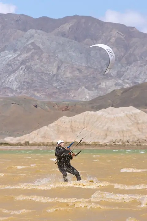 Sesión de navegación con kite blanco y montañas de fondo