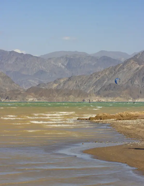 Orilla y agua turquesa del embalse con un kite navegando a lo lejos