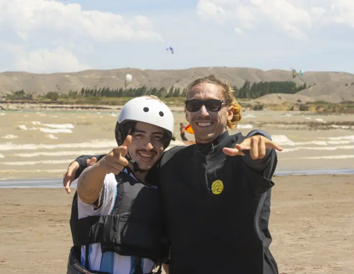 Instructor y alumno con casco sonriendo en la orilla después de una clase